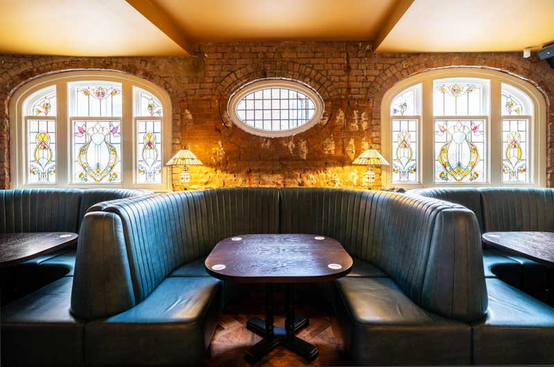 classic-building-group-white-lion-stained-glass-stockport curved seating areas with wooden table in the centre, flanked either side by stunning stain glass